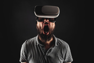 bearded man screaming during the using helmet of virtual reality. Black background