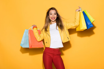 smiling stylish asian woman with shopping bags on yellow background