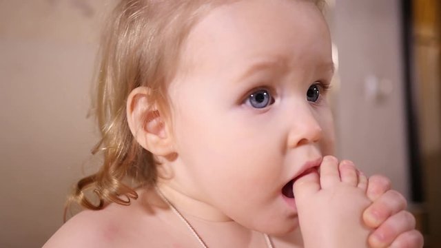 Little baby girl portrait play with her leg sucking biting foot toe putting it in mouth