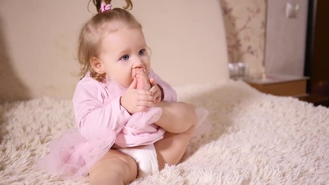 Little baby girl portrait play with her leg sucking biting foot toe putting it in mouth