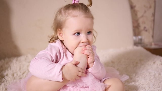 Little baby girl portrait play with her leg sucking biting foot toe putting it in mouth