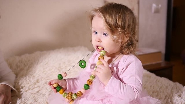 Little baby child girl portrait play at home bite hold in mouth colored beads of mother