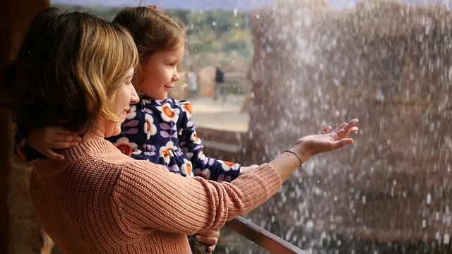Mother holds a child girl happy enjoy water falling in zoo catching drops in slow motion