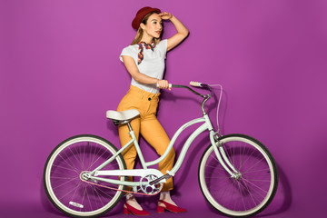Fototapeta na wymiar side view of stylish asian girl standing with bike and looking away isolated on violet