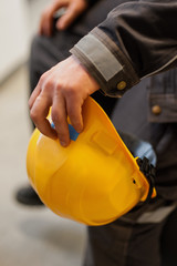 Worker holds yellow protective helmet in his hand