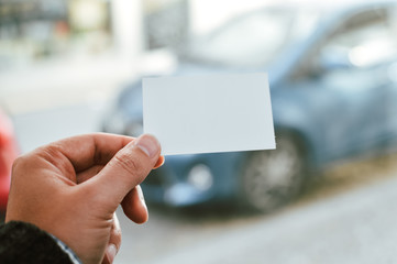 Closeup image of holding business card, person hand showing plain mock up space on car window professional office background. Businessman communication information