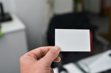 Closeup image of holding business card, person hand showing plain mock up space on professional office background. Businessman communication information