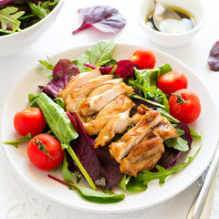 Sliced grilled chicken with green leaves salad on white plate