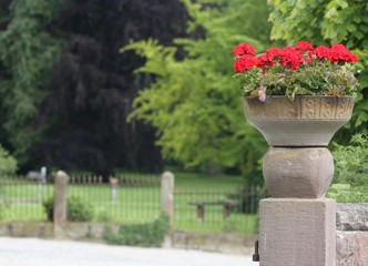 Fototapeta na wymiar A flower arrangement on a old stone column in front of the castle park