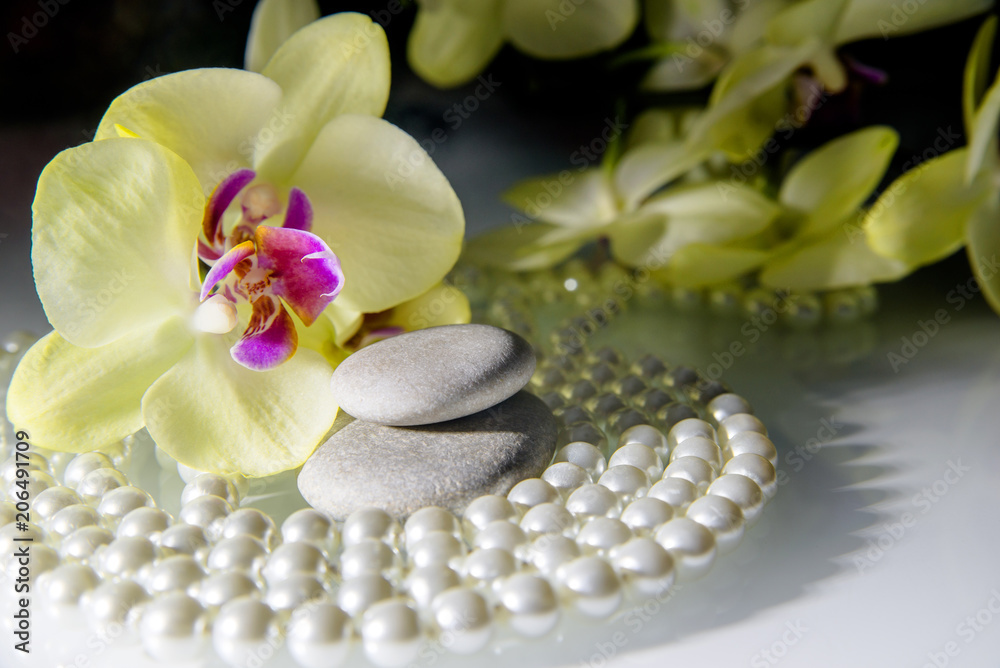 Wall mural flat stones on a white glass on the background of yellow orchids