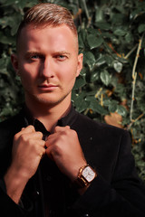 Young and serious businessman wearing T-shirt and black trousers sitting on the street and thinking. Men's fashion.