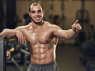 Fototapeta na wymiar Smiling happy young athlete posing and points with your finger in modern gym
