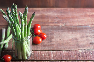 Banches of fresh green asparagus and tomatoes on wooden background