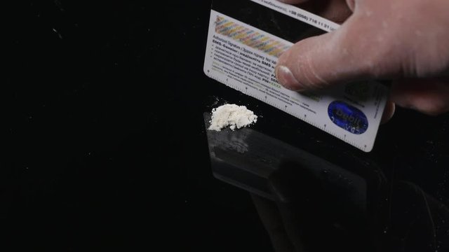 DRUGS: Man does a lines of heroin by plastic card - Close up. Plastic card and white powder. Lines and pile of cocaine on wooden table