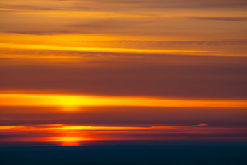 Big red sun circle rises out from behind dark horizon on background varicolored clouds of warmly shades. Beautiful background of dawn on picturesque cloud sky.