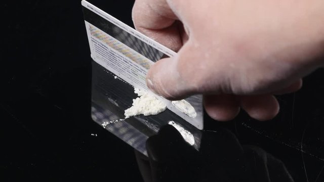 DRUGS: Man does a lines of heroin by plastic card - Close up. Plastic card and white powder. Lines and pile of cocaine on wooden table