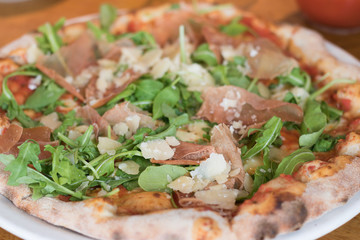 Image of a delicious pizza with ham, cheese and green herb of wild rocket. It is a favorite food of tourists during travel. 