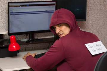 Internet troll with the evil face sitting at the computer. Bad young man with an inscription on his back 