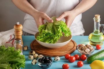 Male hand holds bunch of lettuce above the bowl on wooden table with fresh ingredients.