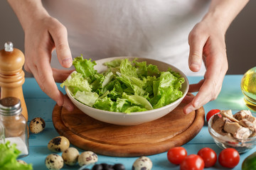 Hands take bowl with lettuce salad leaves from kitchen table with food.