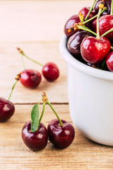 cherries in a white enamel mug on a wooden table, fresh cherry, seasonal berries, sweet cherry, ripe berries, berries in a mug