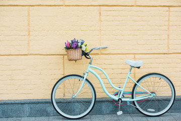 Fototapeta na wymiar white bicycle with beautiful colorful flowers in basket near wall