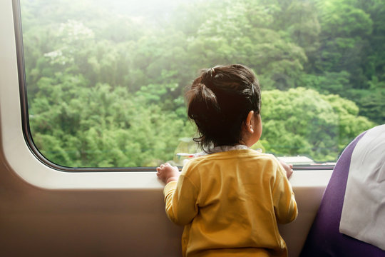 Happy and Excited Kids Traveling by Train. A Two Years old Girl Looking through Wide Glass Window. Green Forest as Outside View