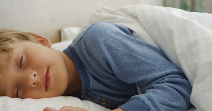 Close up of the cute small blond boy sleeping sweet in a bed in the morning. Inside