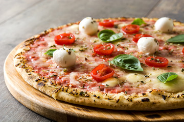 Pizza with tomatoes, cheese and basil on wooden table