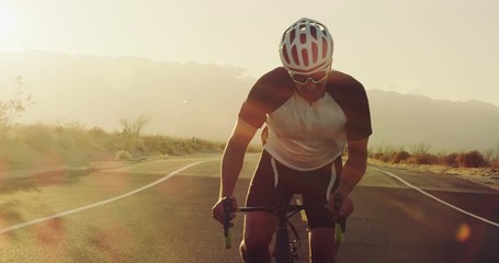Slow motion young man cycling on road bike outside on desert road at sunset with lens flare - Powered by Adobe