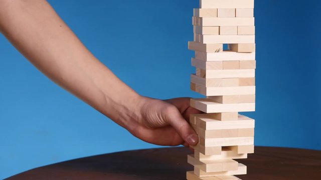 hands of Young man plays jenga on blue background, close-up. A man builds a tower of blocks while playing jenga