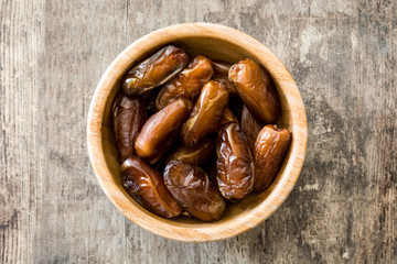 Dates food in wooden bowl on wooden table. Top view