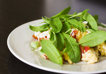 Egg omelet with tomato and fresh arugula spinach in white plate on wooden background