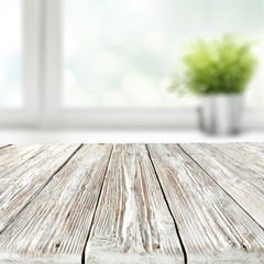 Empty shabby chic wooden styled table with copy space for products and blurred green potted plant...