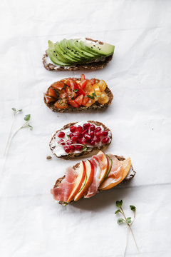 Variety of bruschettas with avecado, prosciutto, tomatoes and pomegranate seeds on white background