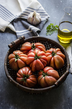 Freshly picked beef tomatoes in a wicker basket against a dark background.