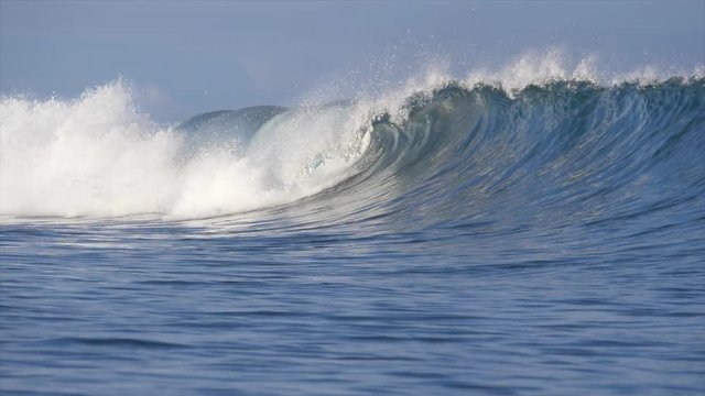 SLOW MOTION: Large barrel wave rolls towards the shore on a beautiful exotic morning. Breathtaking shot of water droplets flying around big tube wave and sparkling in the bright tropical sunshine.