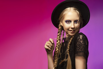 A beautiful smiling blonde teenage girl wearing a black gothic dress and a black hat. Conceptual makeup, red eyelashes and sequins.