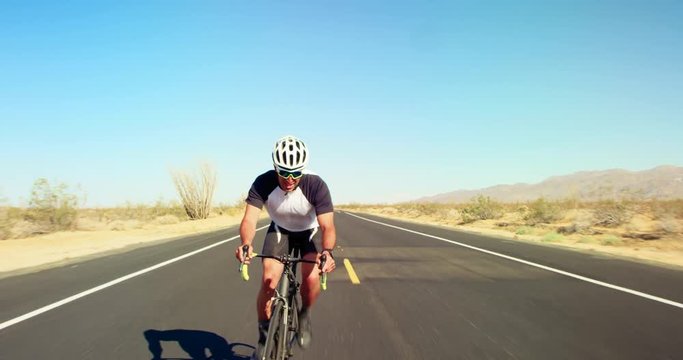 Young healthy man cycling on road bike outside on desert road on sunny day with blue sky in background 