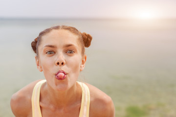 Portrait of young stylish laughing girl model summer natural makeup outside on the beach. Looking at camera showing her tongue