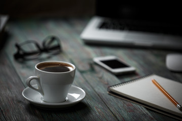 A cup of coffee in the workplace on a wooden table.