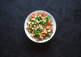 Chickpea salad with vegetables on a black background. Summer vegetarian diet.