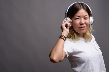 Young beautiful Kazakh woman listening to music against gray bac