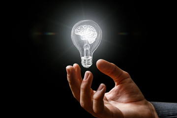 Light bulb with brain burning in the hand .