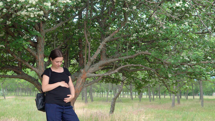 A young, beautiful, pregnant girl, near a tree, in a black T-shirt.