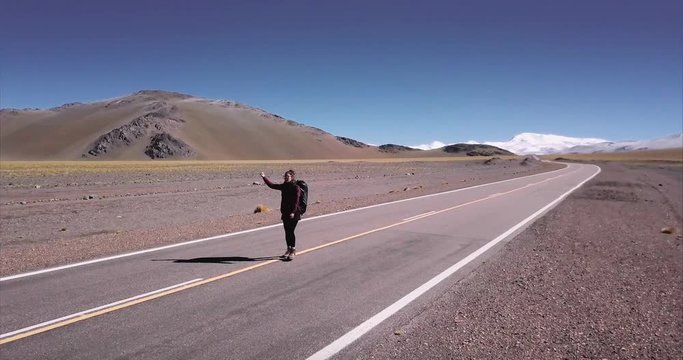 Beautiful young female hitch-hiking by the road in a lonely road of the Andean Range in Argentina. Aerial view, 4k