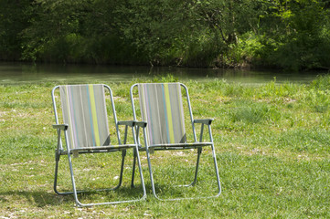 Folding camping chairs on the green lawn by the river