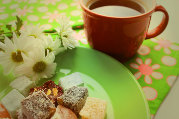 Morning breakfast  with hot tea in a red cup, turkish delights and fresh camomile on green background