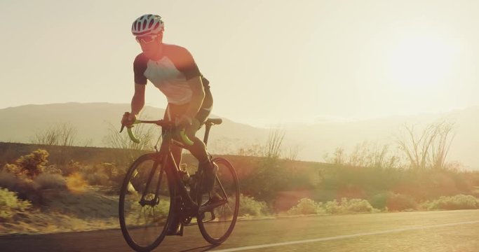 Young man cycling on road bike outside on desert road at sunset with lens flare 
