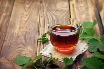 A fragrant herbal tea with mint leaves, lemon balm, raspberries and currants. Close-up. A cup of herbal tea on a wooden background. - obrazy, fototapety, plakaty